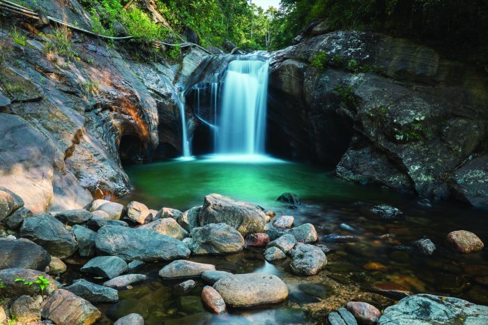 Fotobehang Een stroom van een waterval in het bos tegen een achtergrond van rotsen en stenen