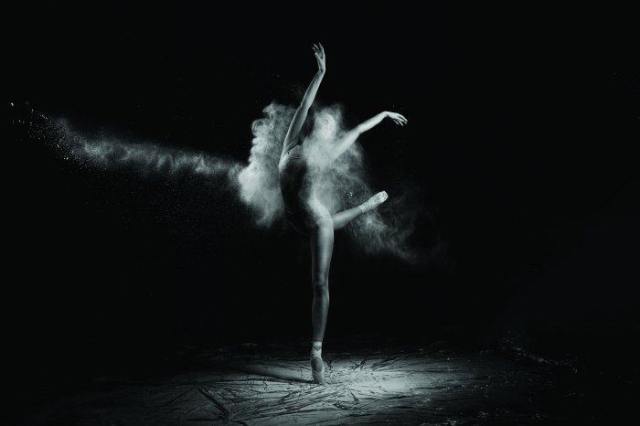 Fotobehang Een elegante balletdanseres in beweging tegen een donkere achtergrond