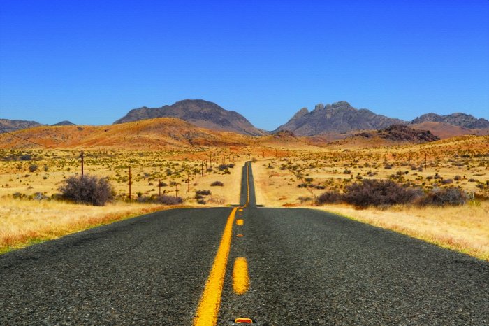 Fotobehang Een rechte betonnen weg die door een uitgestrekte woestijn snijdt