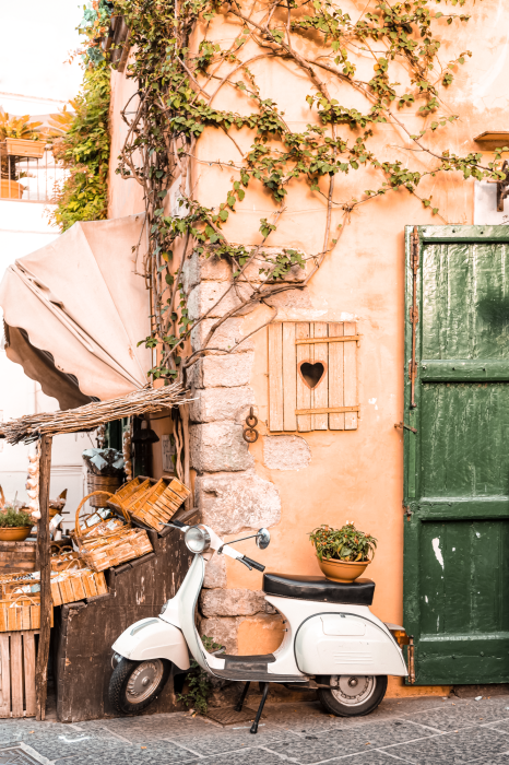 Poster Een witte scooter met op de achtergrond een gebouw met wijnranken