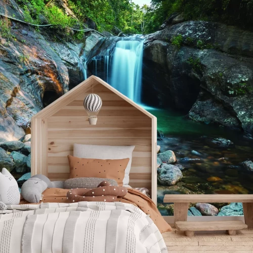 Fotobehang Een stroom van een waterval in het bos tegen een achtergrond van rotsen en stenen