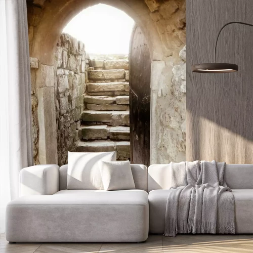 Fotobehang Een stenen muur met een open deur en lichtstralen erachter