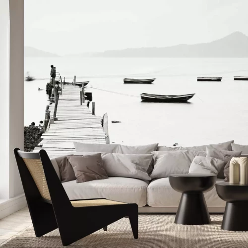 Fotobehang Zwart-witbeeld van een man op een pier en boten op het water