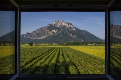 Fotobehang Uitzicht vanaf een open raam, van een berg, met een groen veld aan de voorkant